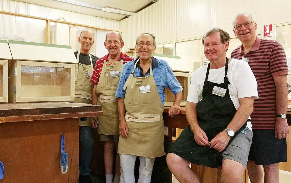 Five Shed members in Bendigo Bank aprons posing with finished bee boxes